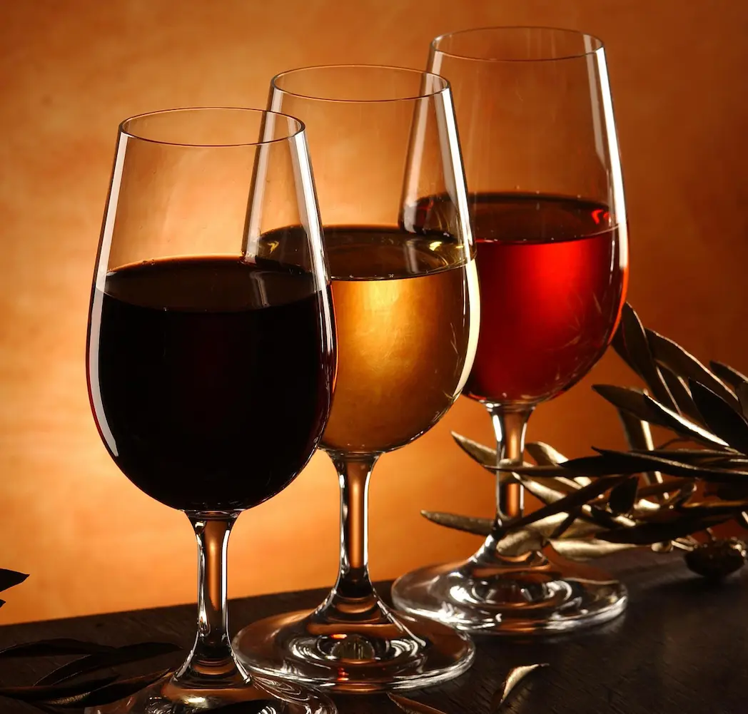 Trois verres de vin alignés sur une table en bois : vin rouge, vin blanc et vin rosé, éclairés par une lumière chaude en arrière-plan – dégustation œnologique, accords mets et vins, ambiance chaleureuse.